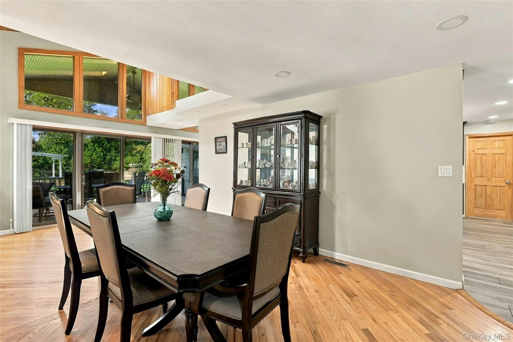 Open-concept dining area featuring wood-finish flooring, vaulted ceilings, expansive multi-pane windows, recessed lighting, and sliding glass doors Open-concept dining area featuring wood-finish flooring, vaulted ceilings, expansive multi-pane windows, recessed lighting, and sliding glass doors