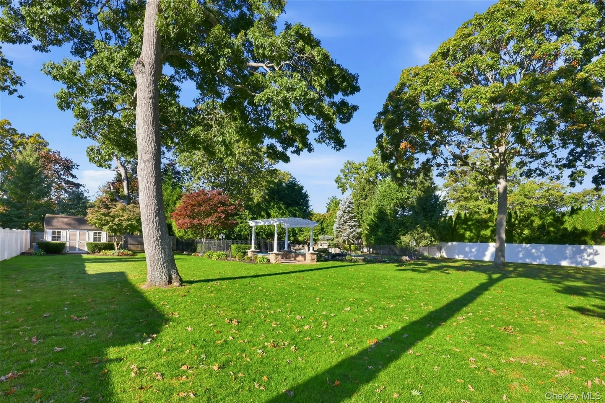 Expansive backyard featuring a white pergola, detached storage structure, mature trees, and perimeter fencing Expansive backyard featuring a white pergola, detached storage structure, mature trees, and perimeter fencing