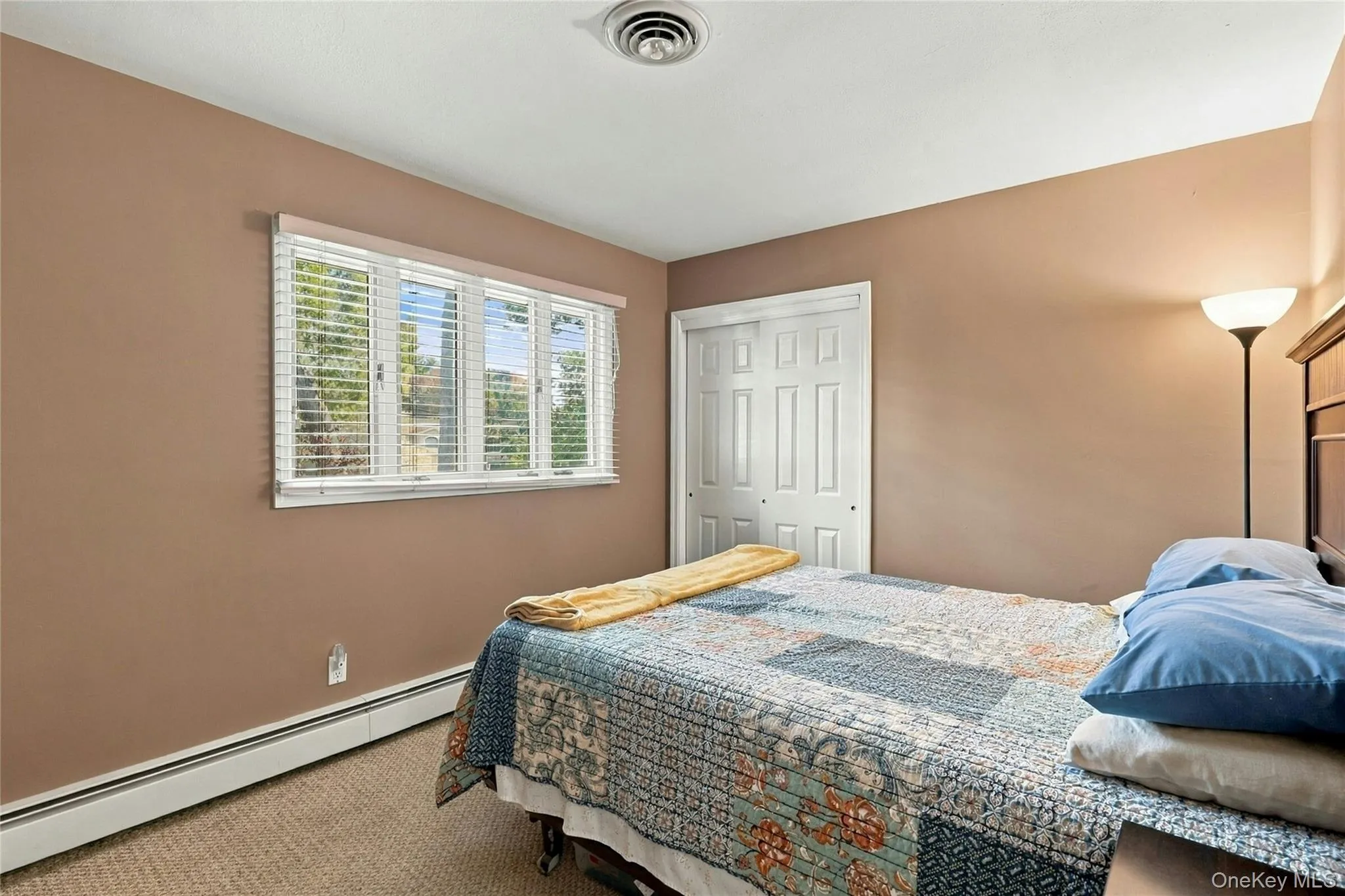 Room featuring neutral wall tones, wall-to-wall carpeting, a multi-pane window with adjustable blinds, and a built-in double-door closet Room featuring neutral wall tones, wall-to-wall carpeting, a multi-pane window with adjustable blinds, and a built-in double-door closet
