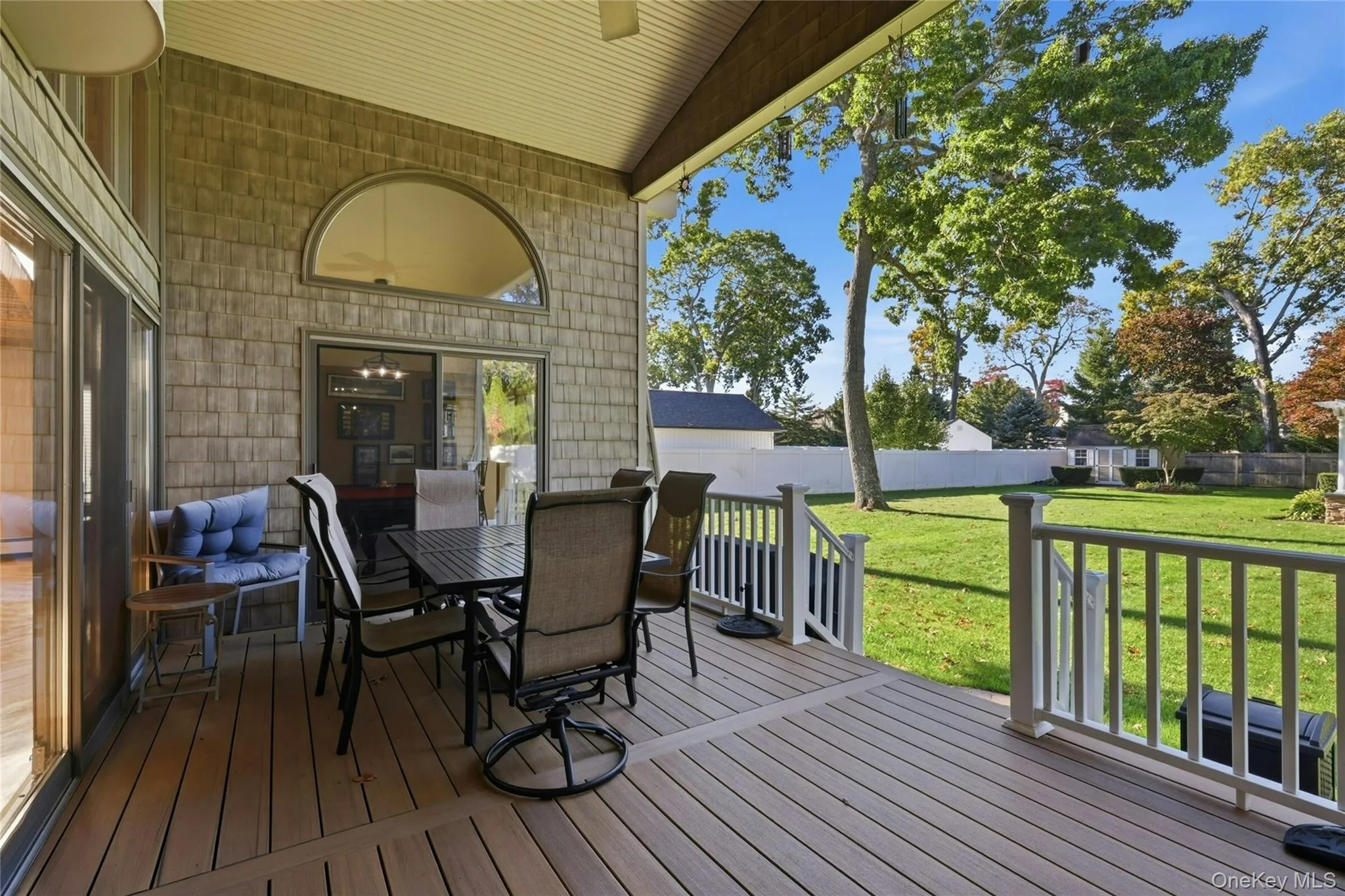 Covered deck featuring composite decking, arched transom window, shingle-style exterior siding, white railing, and expansive lawn Covered deck featuring composite decking, arched transom window, shingle-style exterior siding, white railing, and expansive lawn