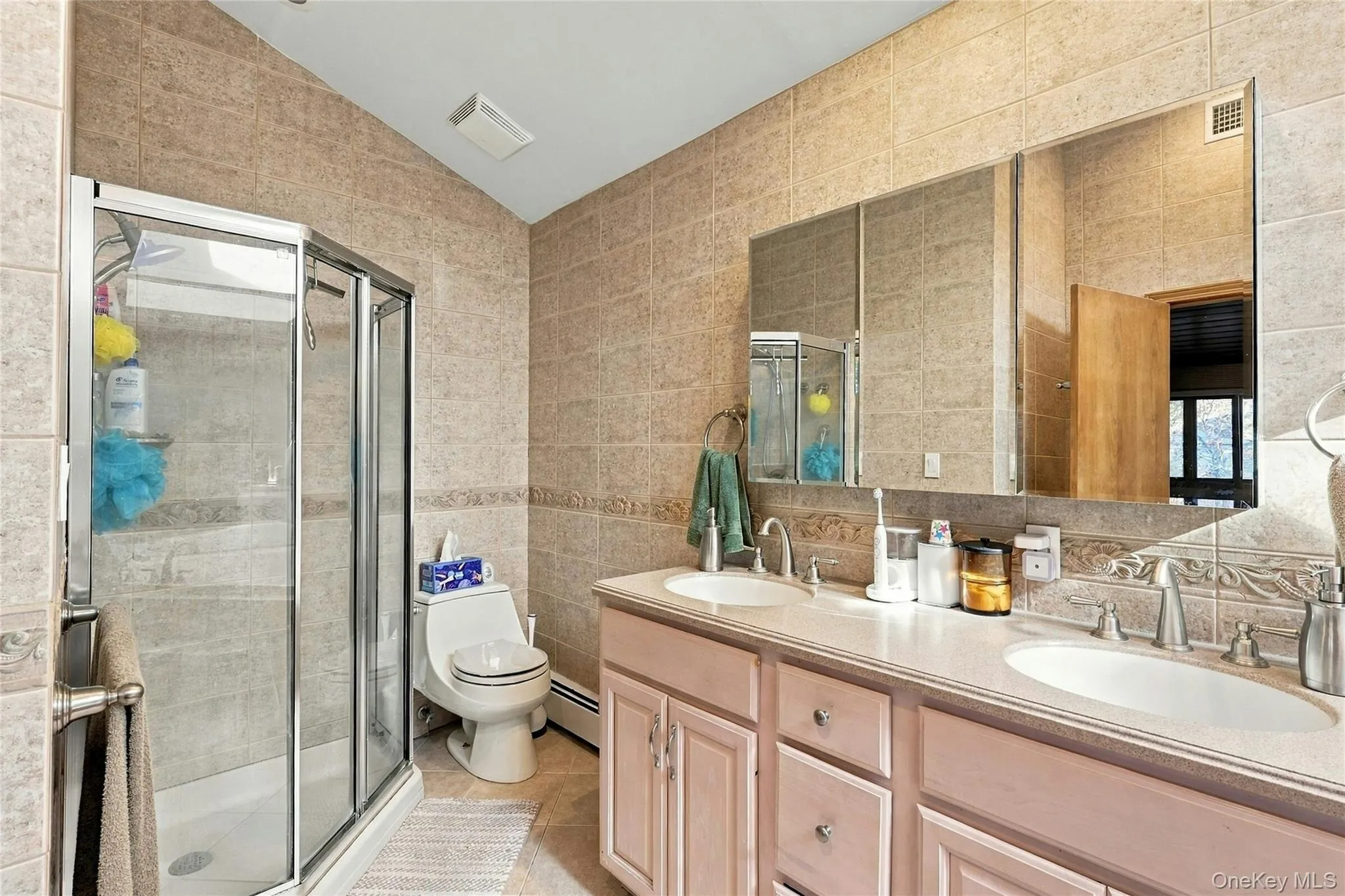 Bathroom featuring a double-sink vanity with a solid-surface countertop, tiled wall surfaces, and a glass-enclosed shower Bathroom featuring a double-sink vanity with a solid-surface countertop, tiled wall surfaces, and a glass-enclosed shower