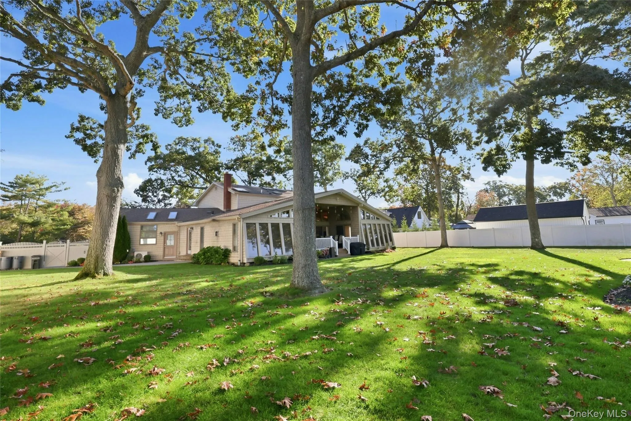 Expansive backyard featuring mature hardwood trees, a manicured lawn, full-height privacy fencing, and a multi-pane glass sunroom addition Expansive backyard featuring mature hardwood trees, a manicured lawn, full-height privacy fencing, and a multi-pane glass sunroom addition