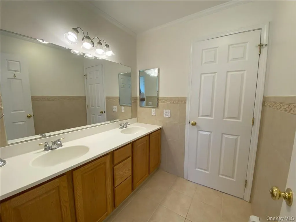 Bathroom with ornamental molding, tile walls, dual bowl vanity, and tile patterned flooring Bathroom with ornamental molding, tile walls, dual bowl vanity, and tile patterned flooring