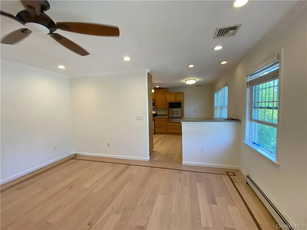 Unfurnished living room with baseboard heating, ceiling fan, light wood-type flooring, and crown molding Unfurnished living room with baseboard heating, ceiling fan, light wood-type flooring, and crown molding