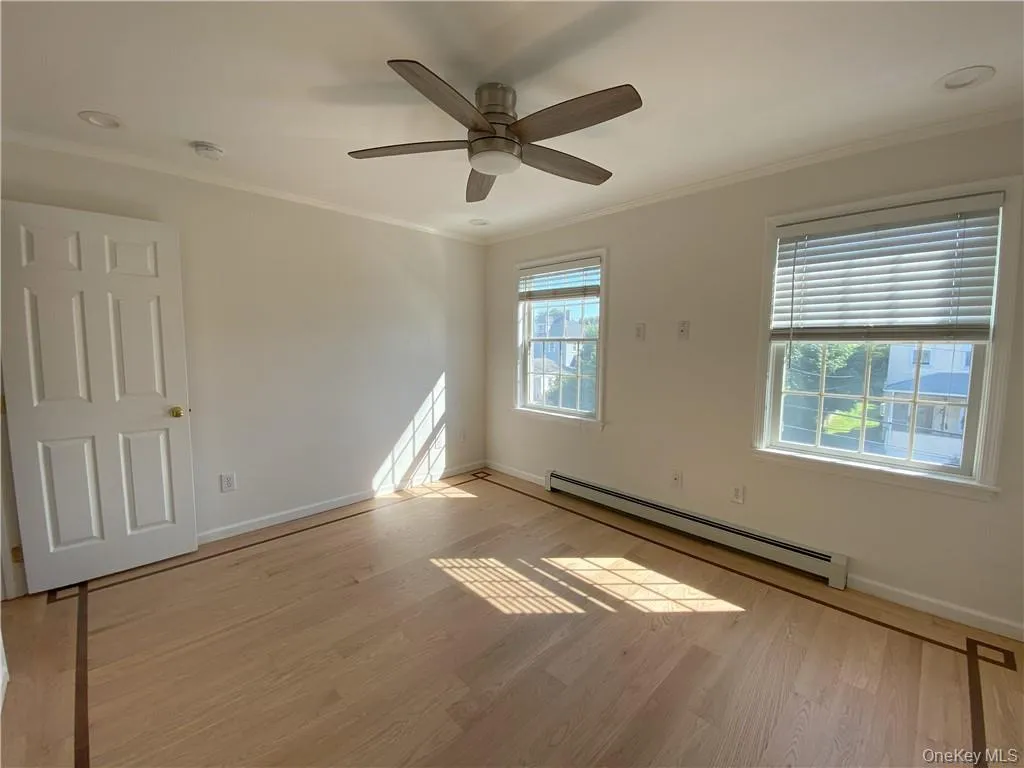 Empty room featuring a baseboard radiator, ceiling fan, light wood-type flooring, and crown molding Empty room featuring a baseboard radiator, ceiling fan, light wood-type flooring, and crown molding