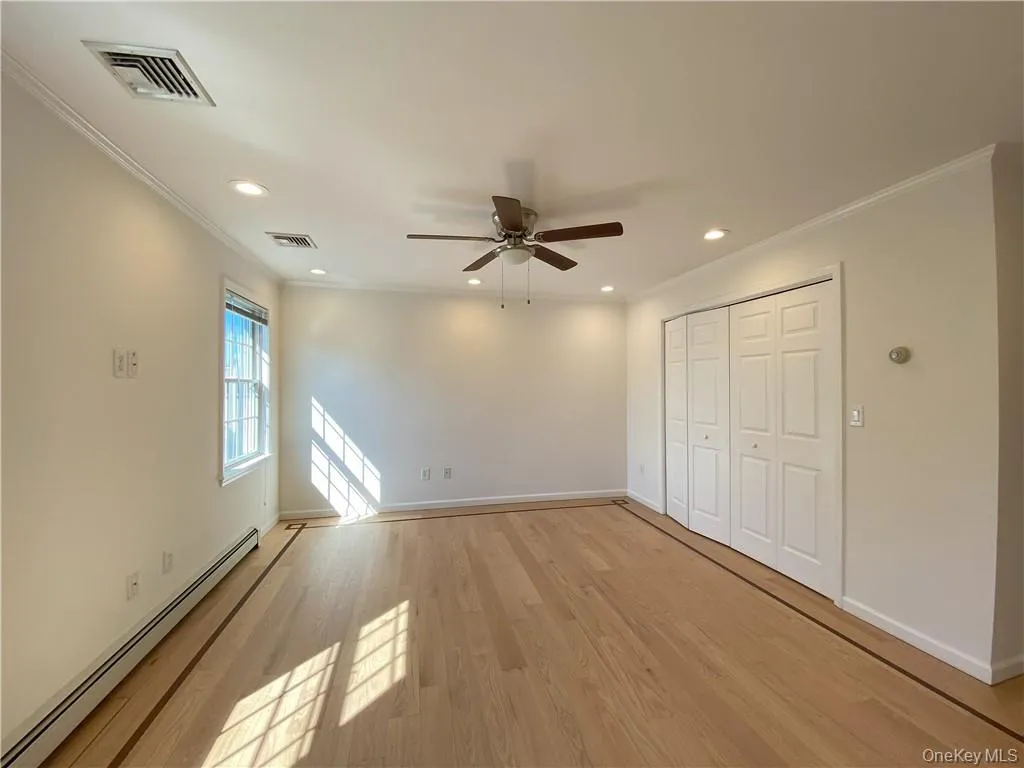Unfurnished bedroom featuring light hardwood / wood-style flooring, baseboard heating, ceiling fan, and crown molding Unfurnished bedroom featuring light hardwood / wood-style flooring, baseboard heating, ceiling fan, and crown molding