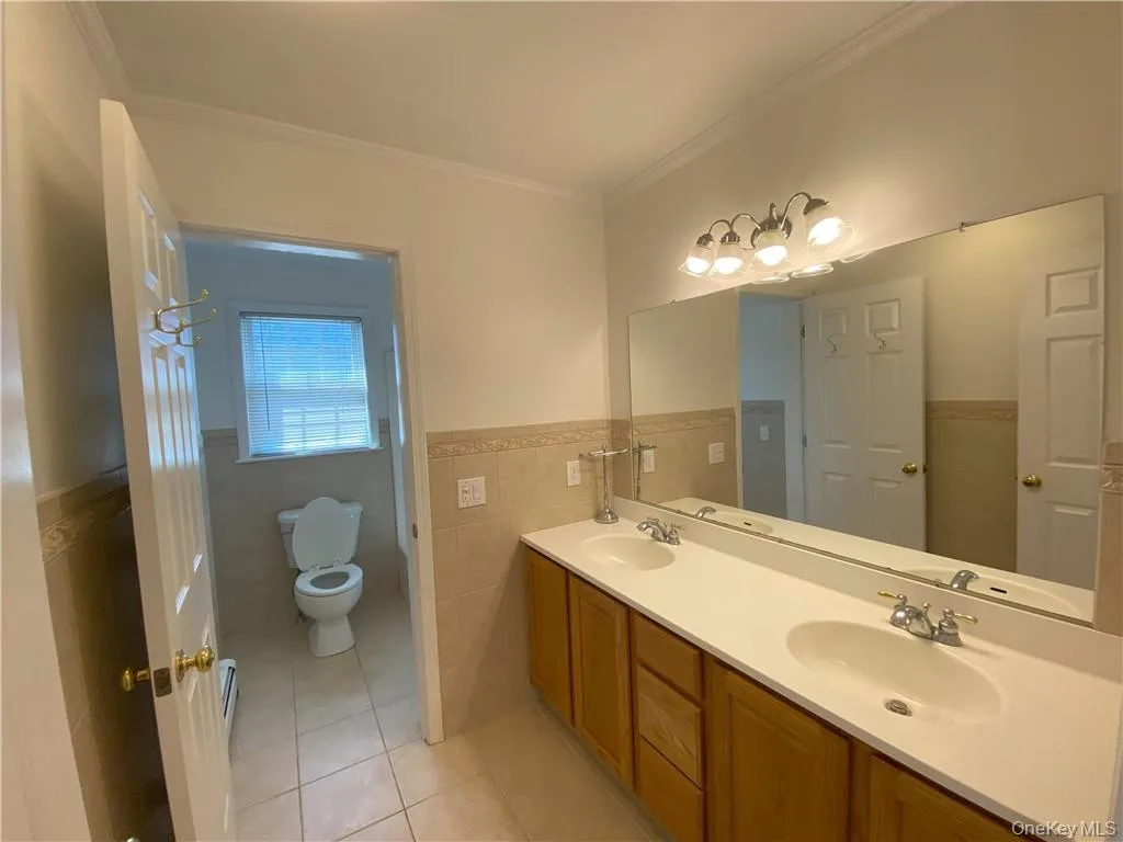 Bathroom featuring dual vanity, tile walls, crown molding, toilet, and tile patterned floors Bathroom featuring dual vanity, tile walls, crown molding, toilet, and tile patterned floors
