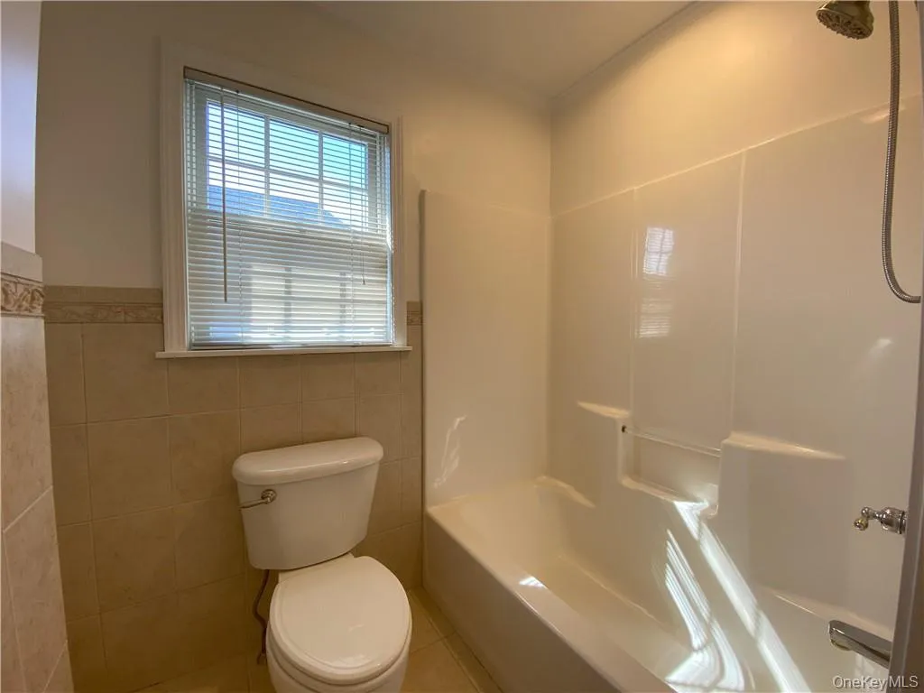 Bathroom with tile patterned floors, shower / washtub combination, tile walls, and toilet Bathroom with tile patterned floors, shower / washtub combination, tile walls, and toilet