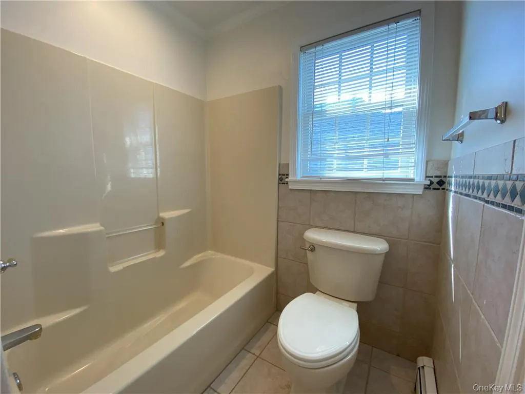 Bathroom featuring tile patterned flooring, tile walls, shower / bathing tub combination, and toilet Bathroom featuring tile patterned flooring, tile walls, shower / bathing tub combination, and toilet