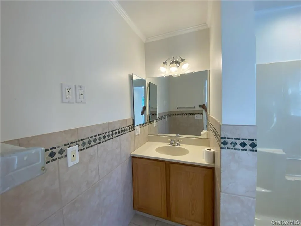 Bathroom featuring vanity, tile patterned flooring, tile walls, and crown molding Bathroom featuring vanity, tile patterned flooring, tile walls, and crown molding