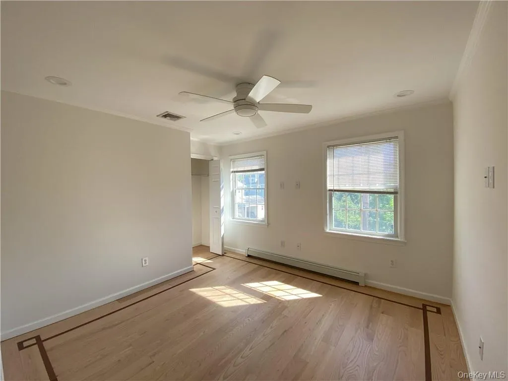 Empty room with light hardwood / wood-style flooring, a baseboard heating unit, crown molding, and ceiling fan Empty room with light hardwood / wood-style flooring, a baseboard heating unit, crown molding, and ceiling fan