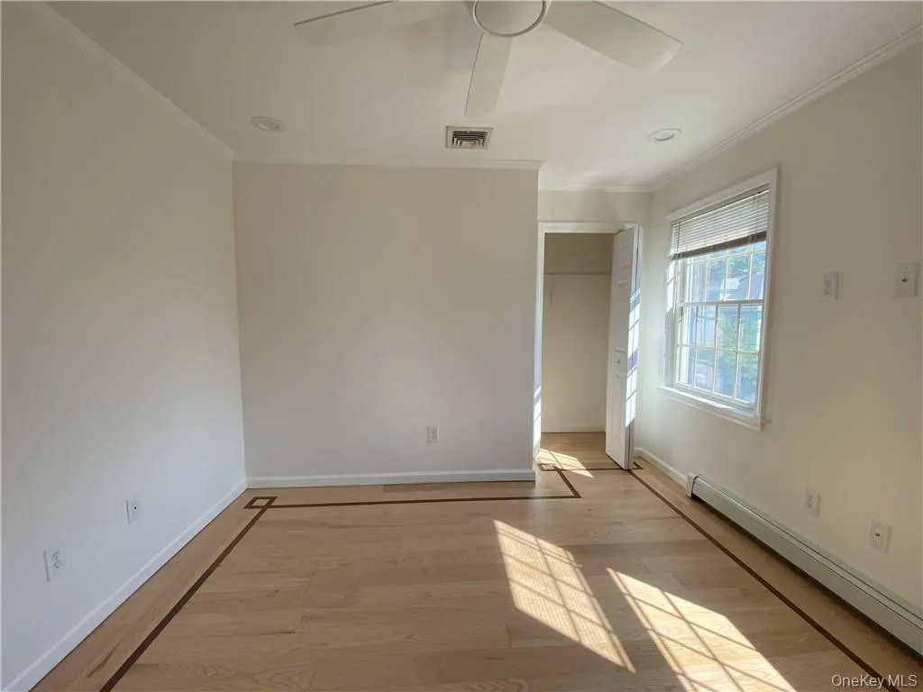 Unfurnished bedroom featuring a closet, baseboard heating, ceiling fan, wood-type flooring, and ornamental molding Unfurnished bedroom featuring a closet, baseboard heating, ceiling fan, wood-type flooring, and ornamental molding