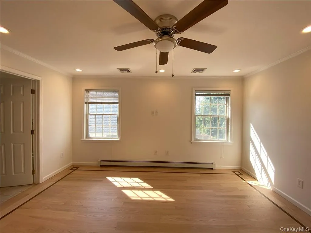 Empty room with a baseboard radiator, ceiling fan, light wood-type flooring, and crown molding Empty room with a baseboard radiator, ceiling fan, light wood-type flooring, and crown molding