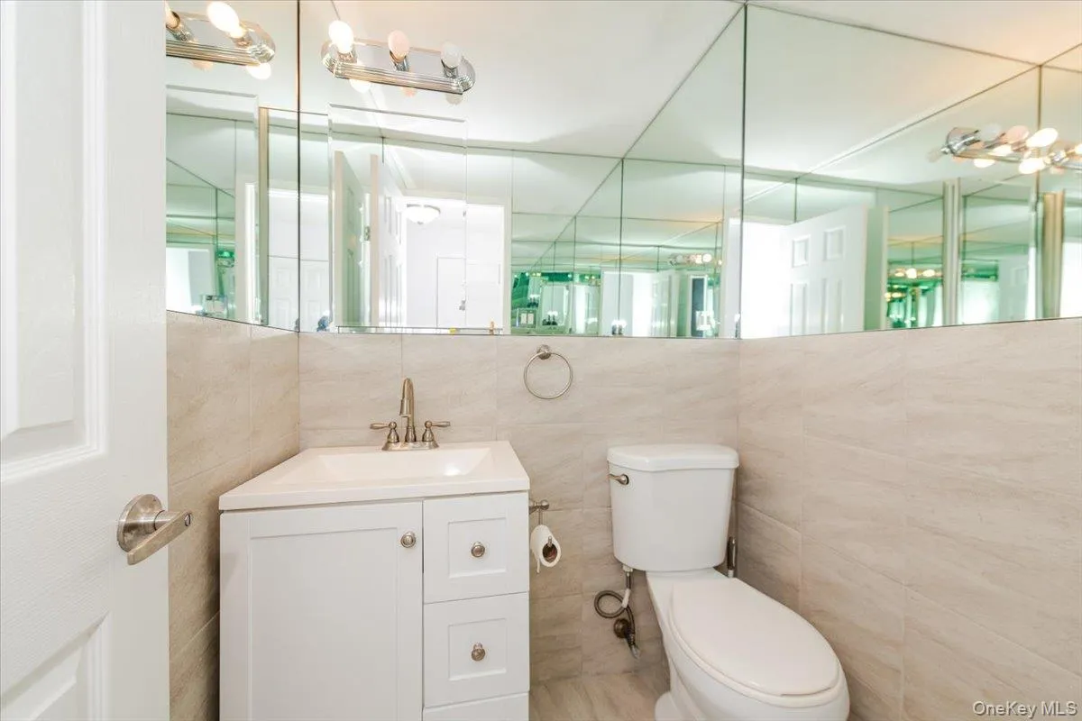 Bathroom featuring toilet, vanity, and tile walls Bathroom featuring toilet, vanity, and tile walls