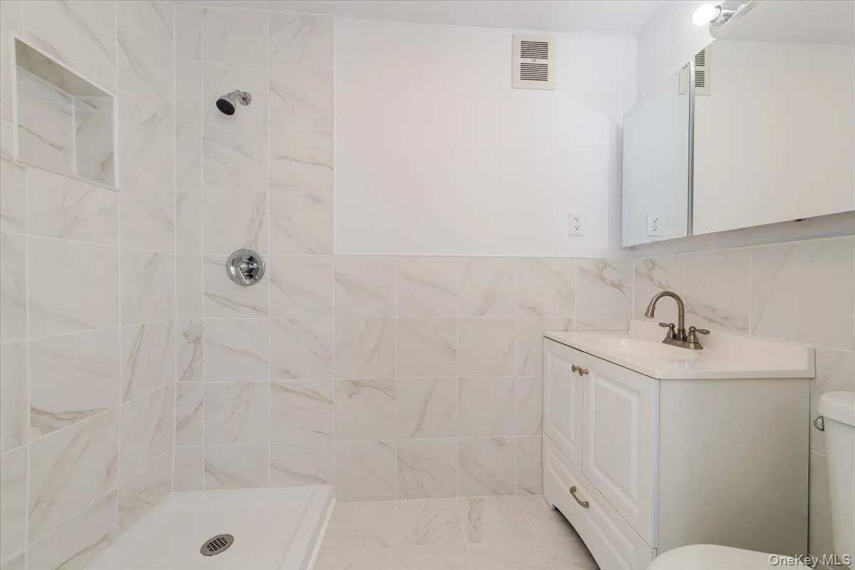 Bathroom featuring tiled shower, vanity, visible vents, and toilet Bathroom featuring tiled shower, vanity, visible vents, and toilet