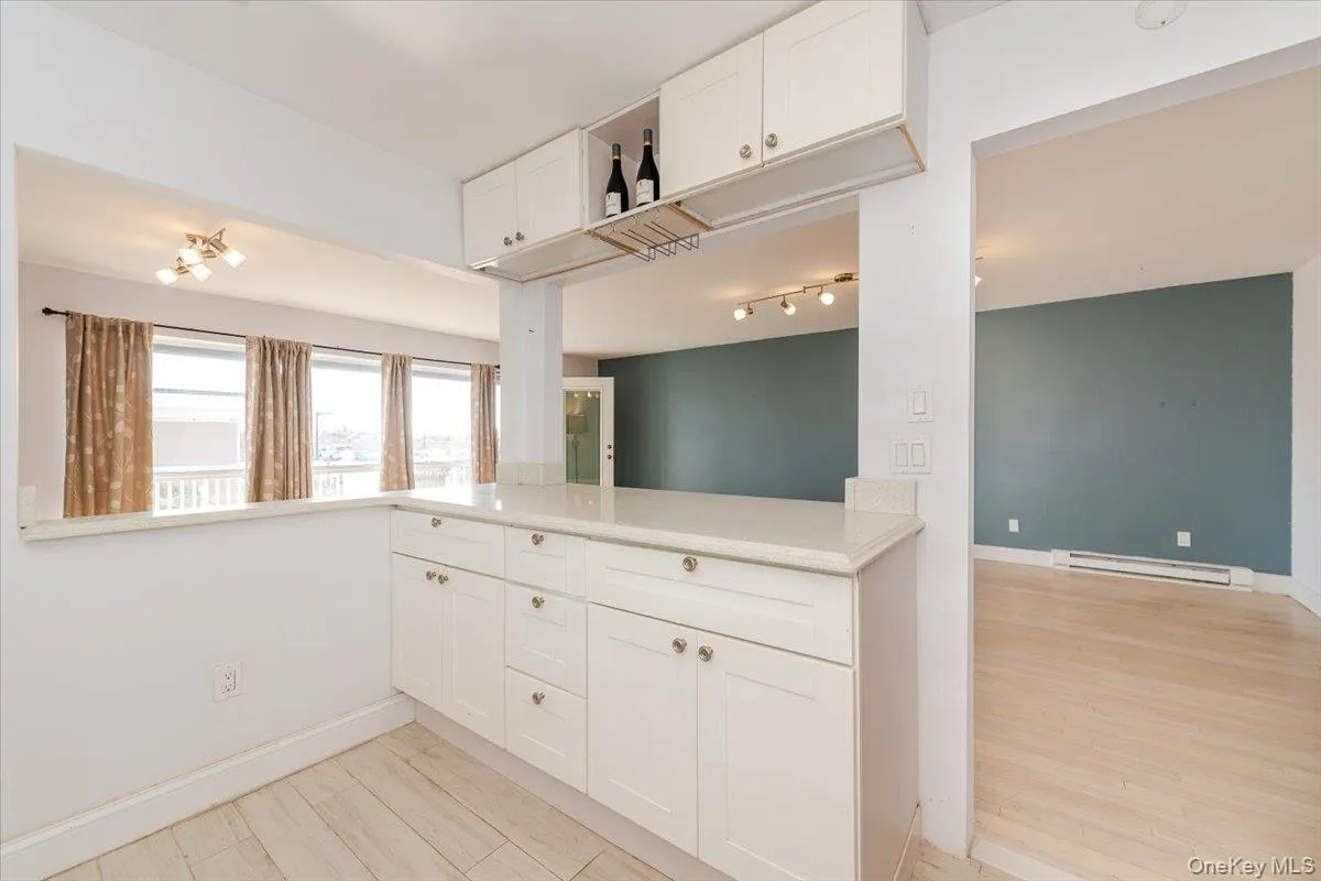 Kitchen featuring baseboard heating, white cabinetry, baseboards, and light countertops Kitchen featuring baseboard heating, white cabinetry, baseboards, and light countertops