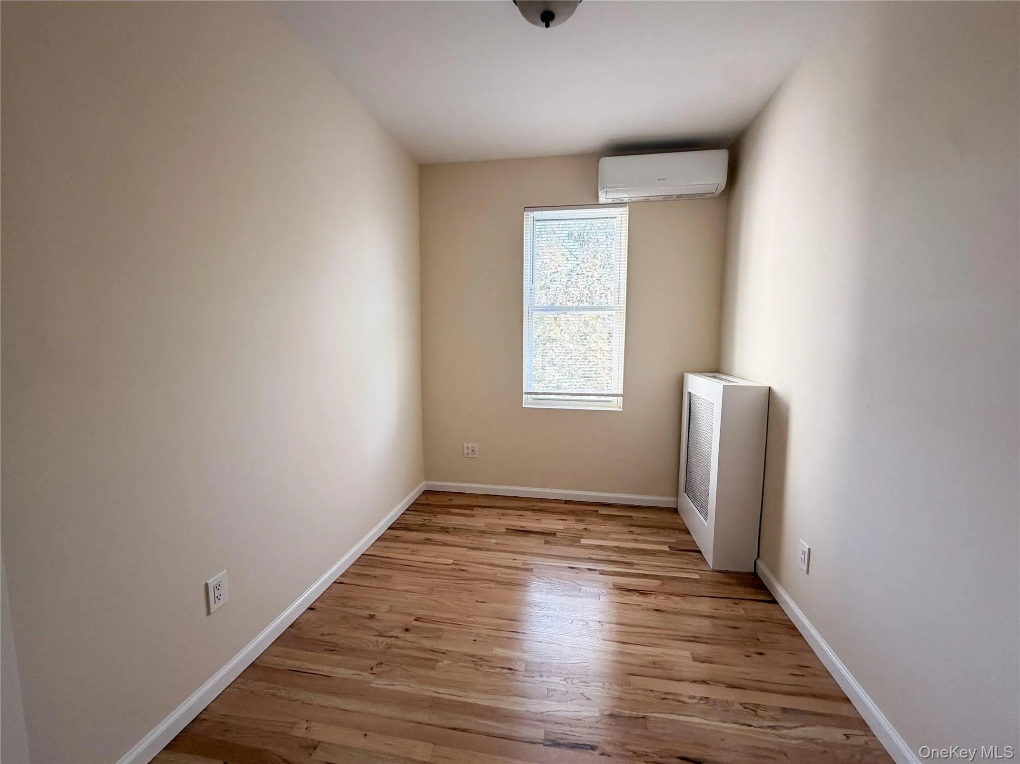 Interior room featuring wood-finish flooring, a single-pane window, and a wall-mounted climate control unit. Interior room featuring wood-finish flooring, a single-pane window, and a wall-mounted climate control unit.