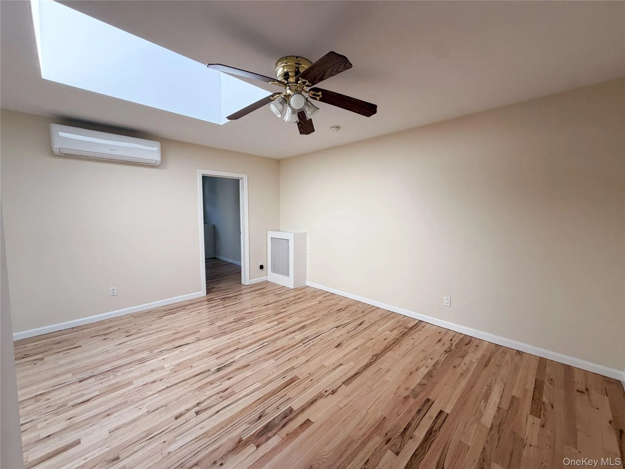 Interior space featuring wood-finish flooring, a rectangular skylight, a wall-mounted ductless air conditioning unit, a ceiling fan with integrated light fixture, and a built-in cabinet. Interior space featuring wood-finish flooring, a rectangular skylight, a wall-mounted ductless air conditioning unit, a ceiling fan with integrated light fixture, and a built-in cabinet.
