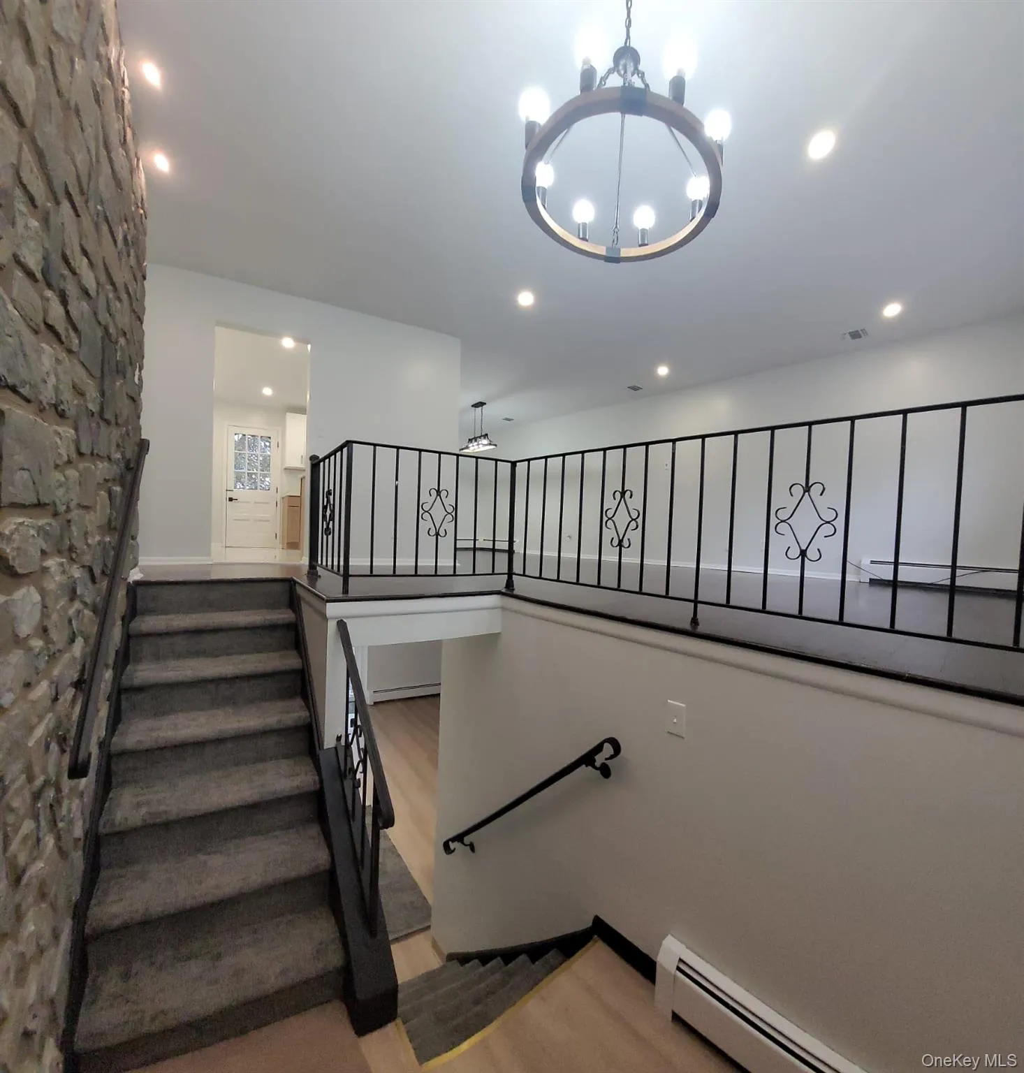 Stairway with hardwood / wood-style floors, a notable chandelier, and a baseboard heating unit Stairway with hardwood / wood-style floors, a notable chandelier, and a baseboard heating unit