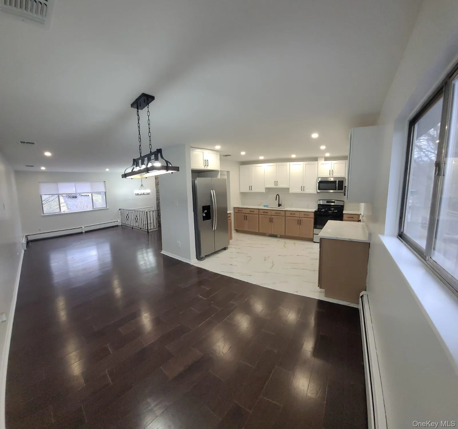 Kitchen featuring a baseboard heating unit, sink, decorative light fixtures, white cabinetry, and stainless steel appliances Kitchen featuring a baseboard heating unit, sink, decorative light fixtures, white cabinetry, and stainless steel appliances