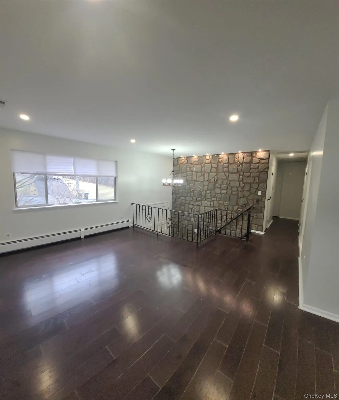 Empty room featuring baseboard heating, a fireplace, dark wood-type flooring, and an inviting chandelier Empty room featuring baseboard heating, a fireplace, dark wood-type flooring, and an inviting chandelier