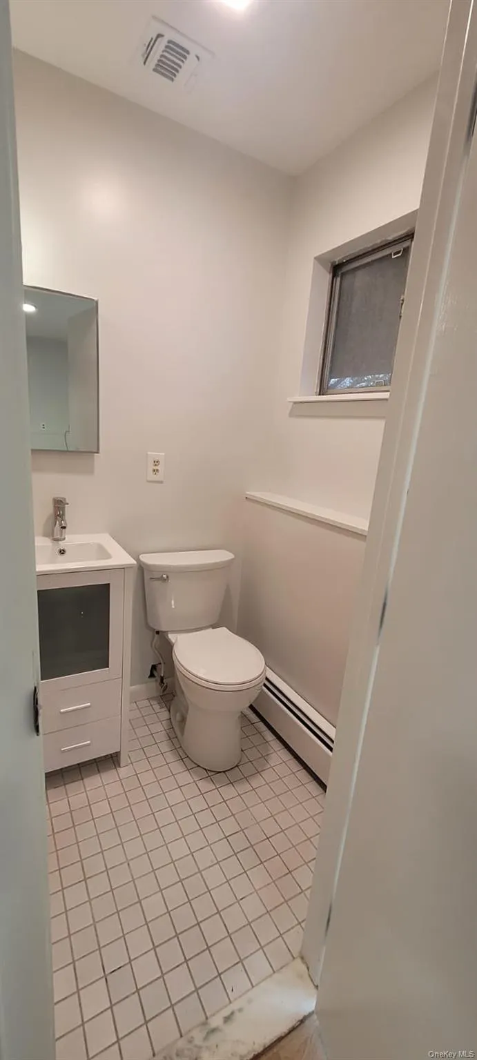 Bathroom featuring toilet, vanity, a baseboard radiator, and tile patterned floors Bathroom featuring toilet, vanity, a baseboard radiator, and tile patterned floors