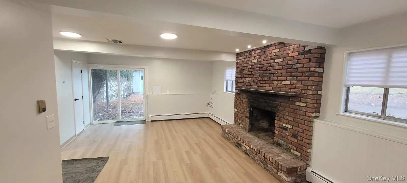Unfurnished living room featuring a fireplace, light hardwood / wood-style floors, and a baseboard heating unit Unfurnished living room featuring a fireplace, light hardwood / wood-style floors, and a baseboard heating unit