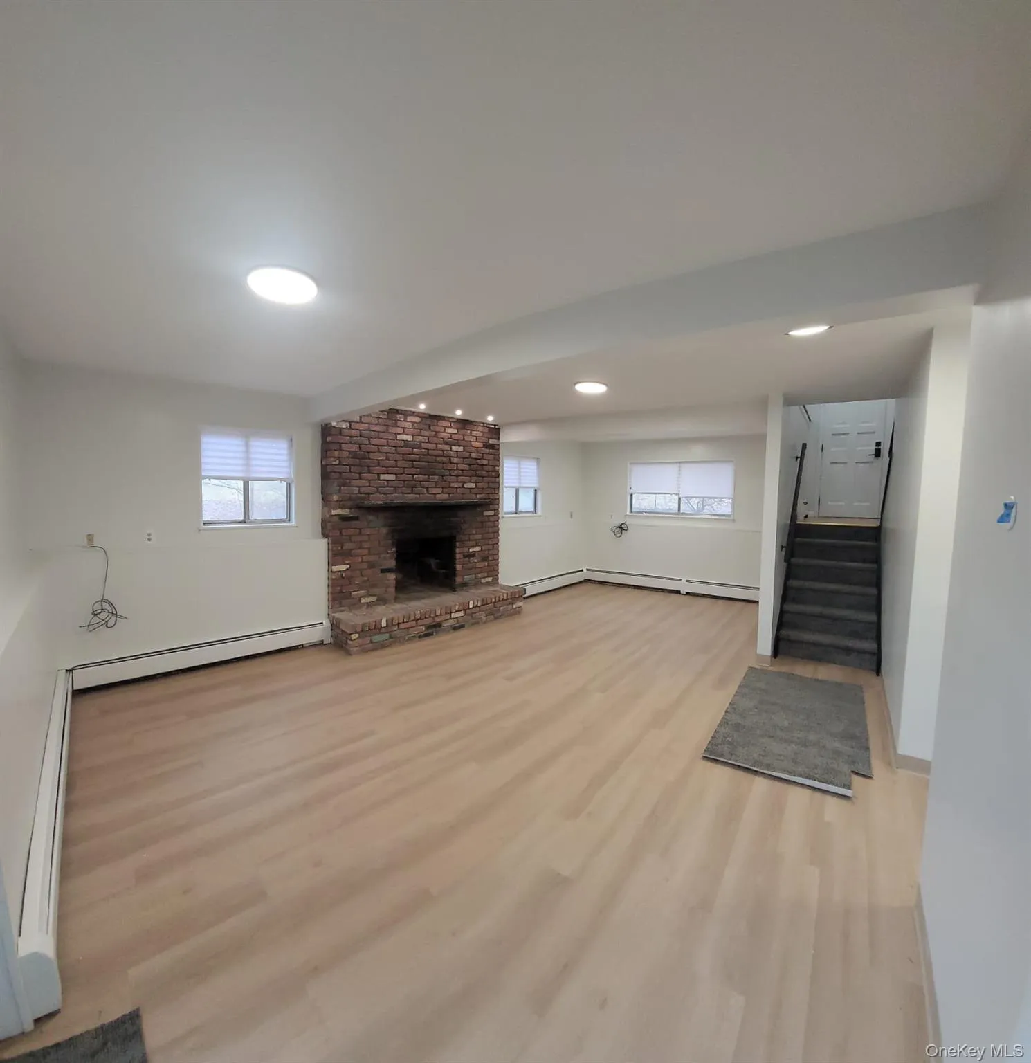 Unfurnished living room with light wood-type flooring, a baseboard radiator, and a brick fireplace Unfurnished living room with light wood-type flooring, a baseboard radiator, and a brick fireplace