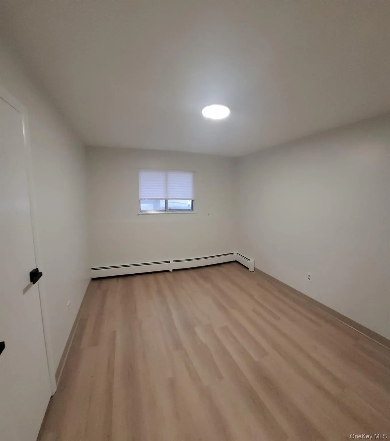 Empty room with light hardwood / wood-style flooring and a baseboard radiator Empty room with light hardwood / wood-style flooring and a baseboard radiator