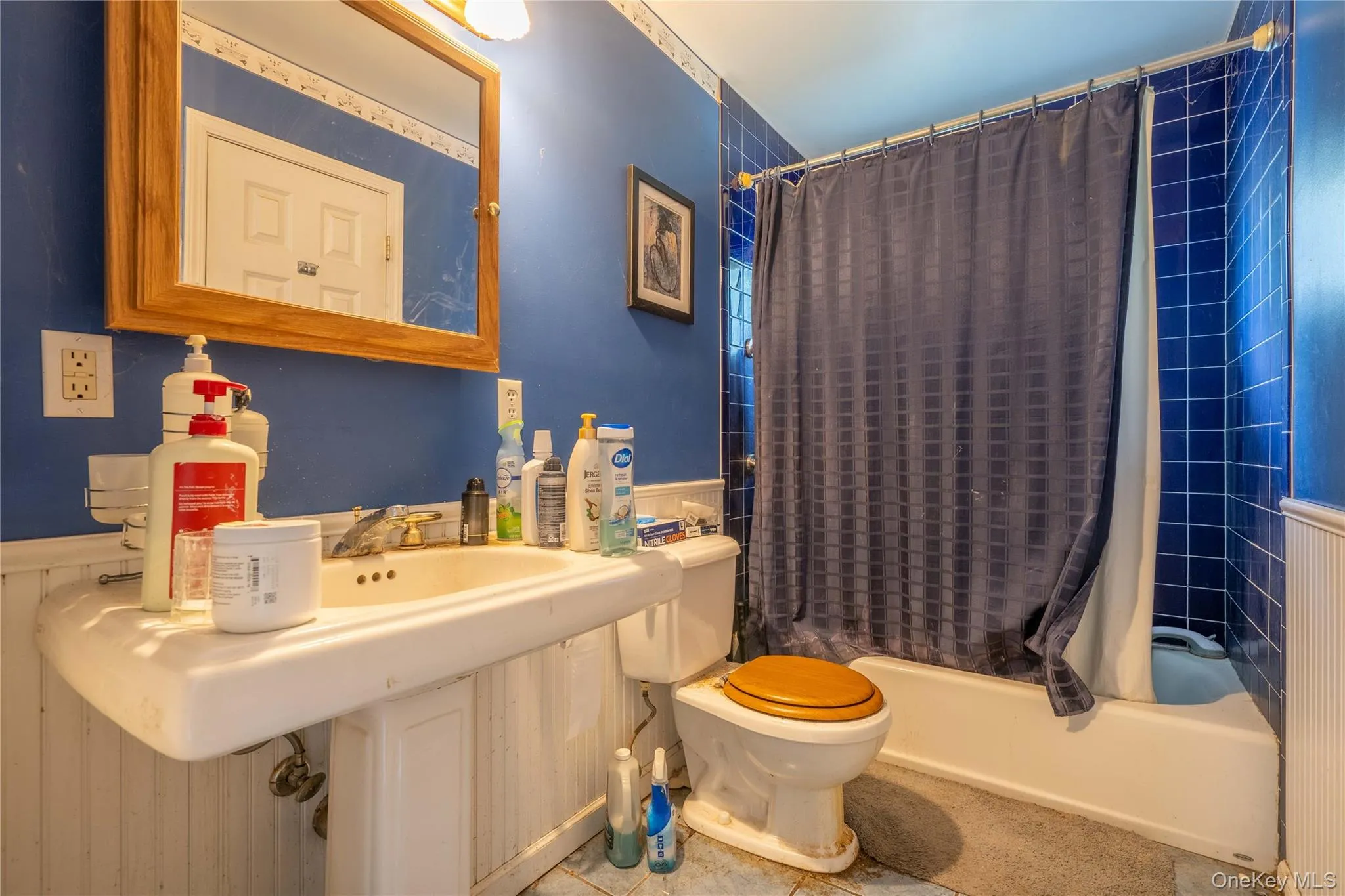Wall-mounted pedestal sink, wood-framed mirror, and floor-to-ceiling tile shower surround with tub combination Wall-mounted pedestal sink, wood-framed mirror, and floor-to-ceiling tile shower surround with tub combination