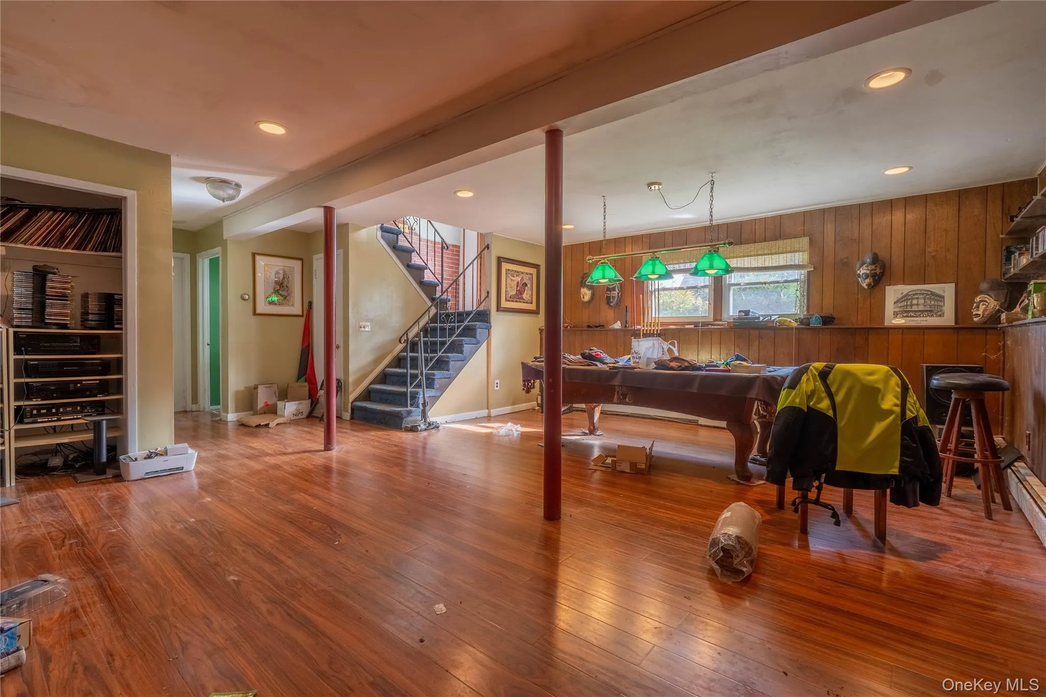 Wood-paneled wall treatments, wood-finish flooring, recessed ceiling lighting, three-light hanging fixture, and built-in wall shelving Wood-paneled wall treatments, wood-finish flooring, recessed ceiling lighting, three-light hanging fixture, and built-in wall shelving