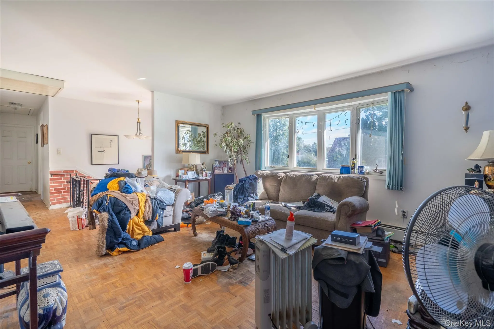 Living area featuring parquet wood-finish flooring, a large multi-pane bay window, and a decorative brick accent wall Living area featuring parquet wood-finish flooring, a large multi-pane bay window, and a decorative brick accent wall