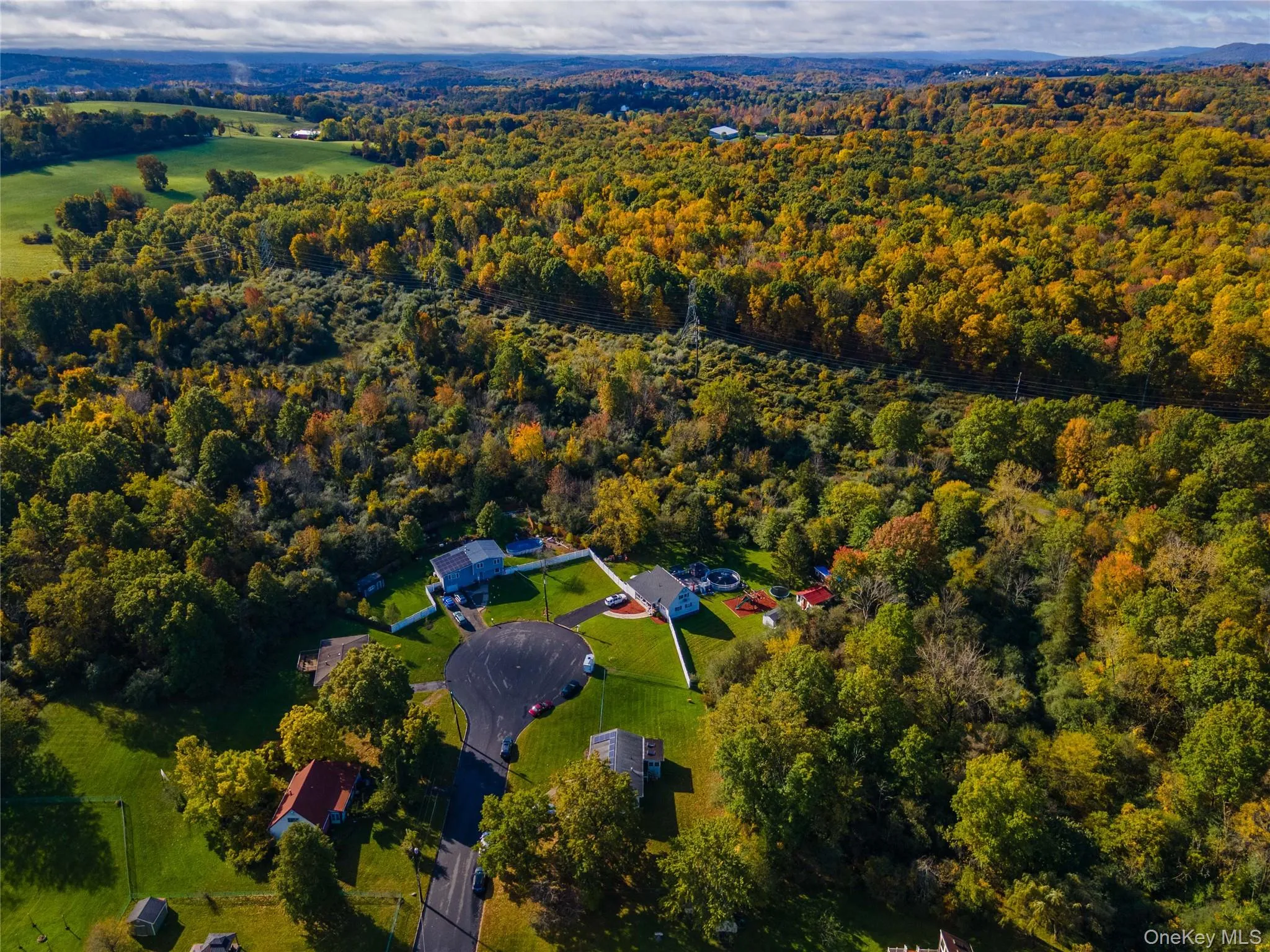 Aerial view of a residential property featuring an asphalt cul-de-sac, expansive lawn, white perimeter fencing, and mature trees Aerial view of a residential property featuring an asphalt cul-de-sac, expansive lawn, white perimeter fencing, and mature trees