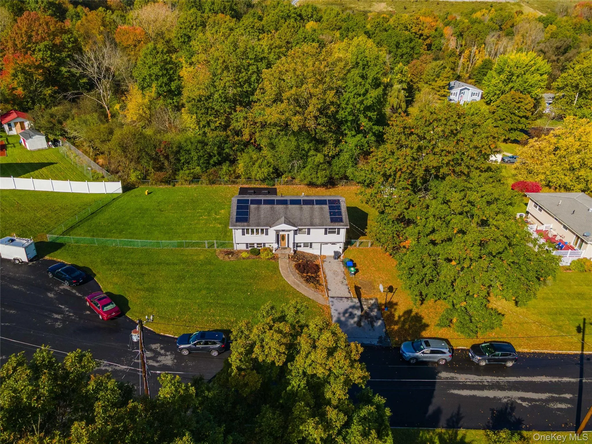 Aerial perspective of a detached residence featuring a roof-mounted solar panel array, an expansive lawn, and a chain-link fenced perimeter Aerial perspective of a detached residence featuring a roof-mounted solar panel array, an expansive lawn, and a chain-link fenced perimeter