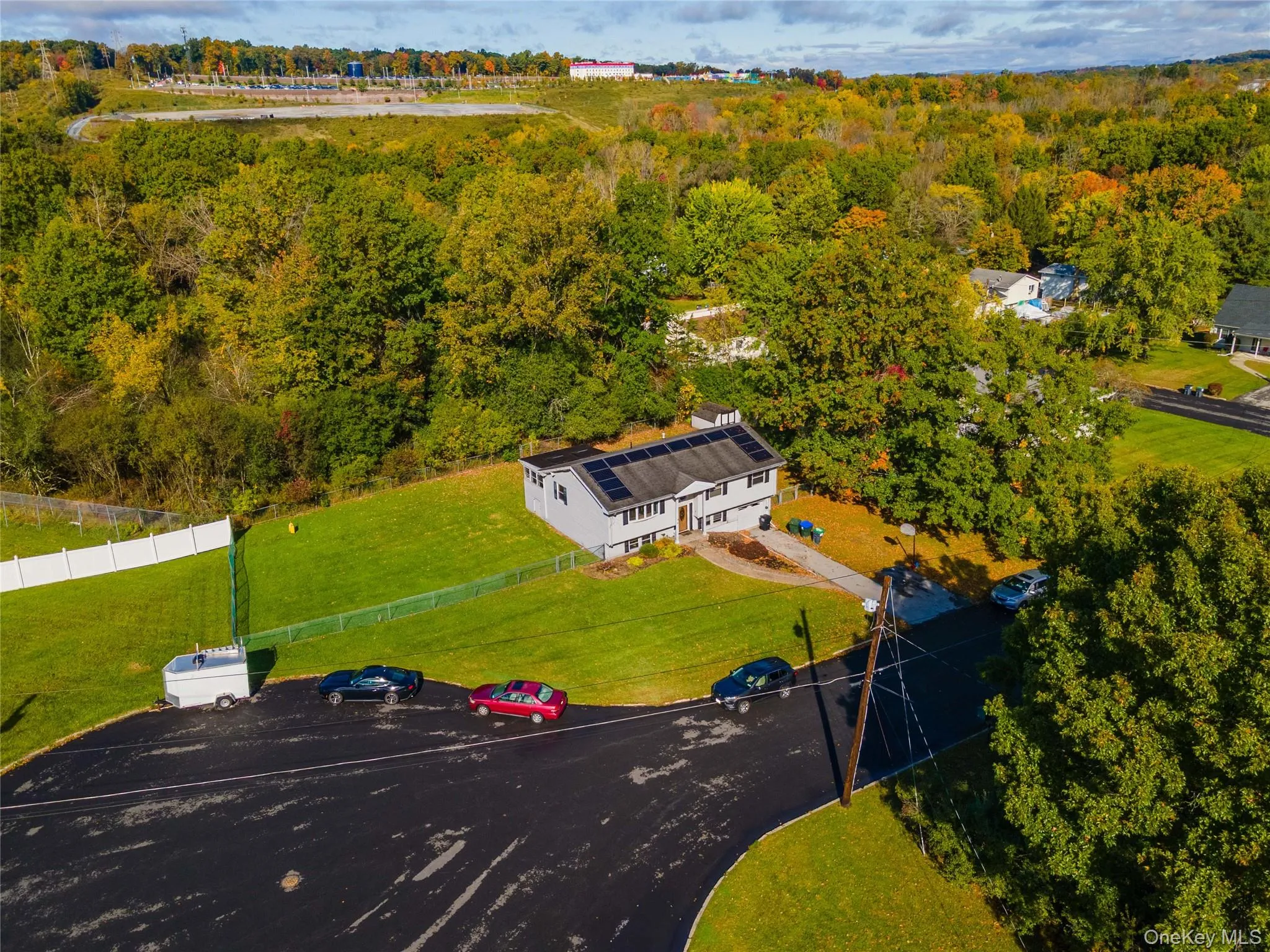 Split-level residence featuring solar panels, a paved driveway, and a chain-link fenced yard situated on a lot with mature trees Split-level residence featuring solar panels, a paved driveway, and a chain-link fenced yard situated on a lot with mature trees