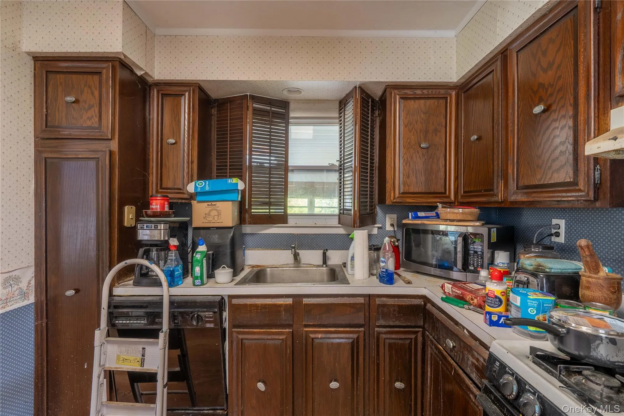Kitchen featuring dark wood cabinetry, integrated appliances, a stainless steel sink, and louvered shutters Kitchen featuring dark wood cabinetry, integrated appliances, a stainless steel sink, and louvered shutters