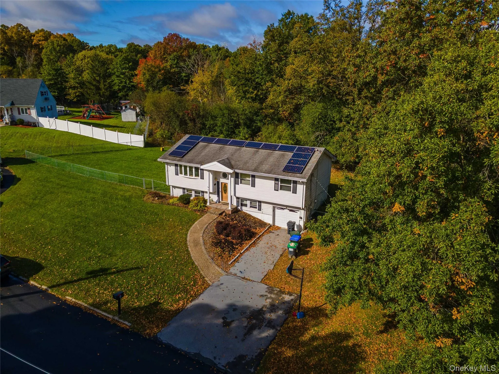 Split-level exterior featuring solar panel roof installation, an attached garage, a paved driveway, and established surrounding greenery Split-level exterior featuring solar panel roof installation, an attached garage, a paved driveway, and established surrounding greenery