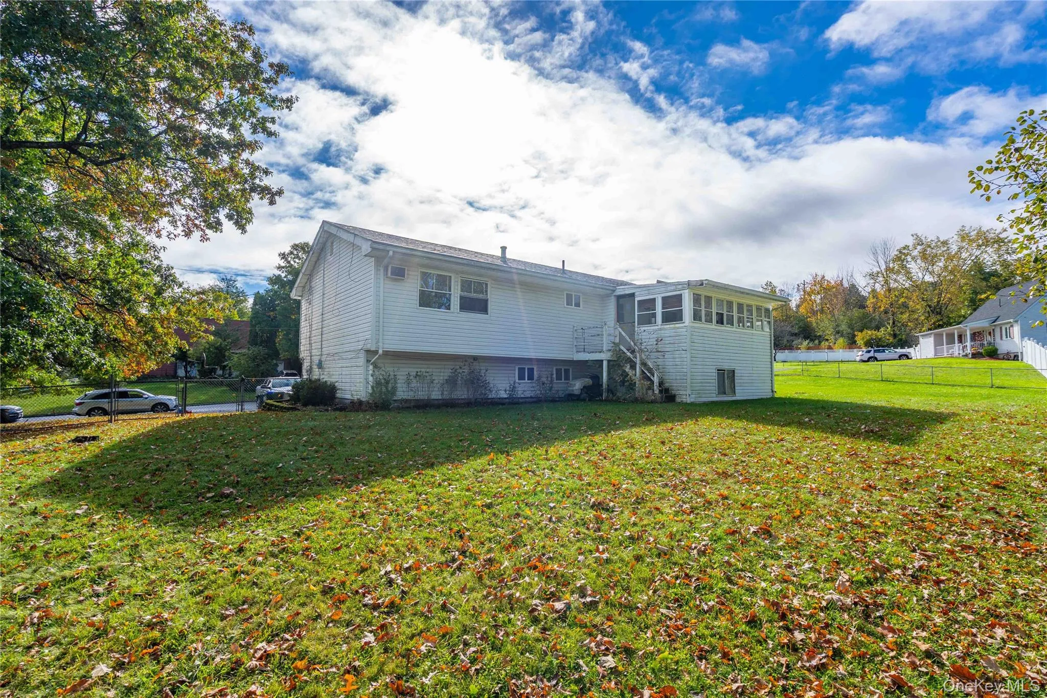 Expansive rear yard featuring a manicured lawn, white horizontal siding, an enclosed sunroom, and an elevated exterior staircase Expansive rear yard featuring a manicured lawn, white horizontal siding, an enclosed sunroom, and an elevated exterior staircase
