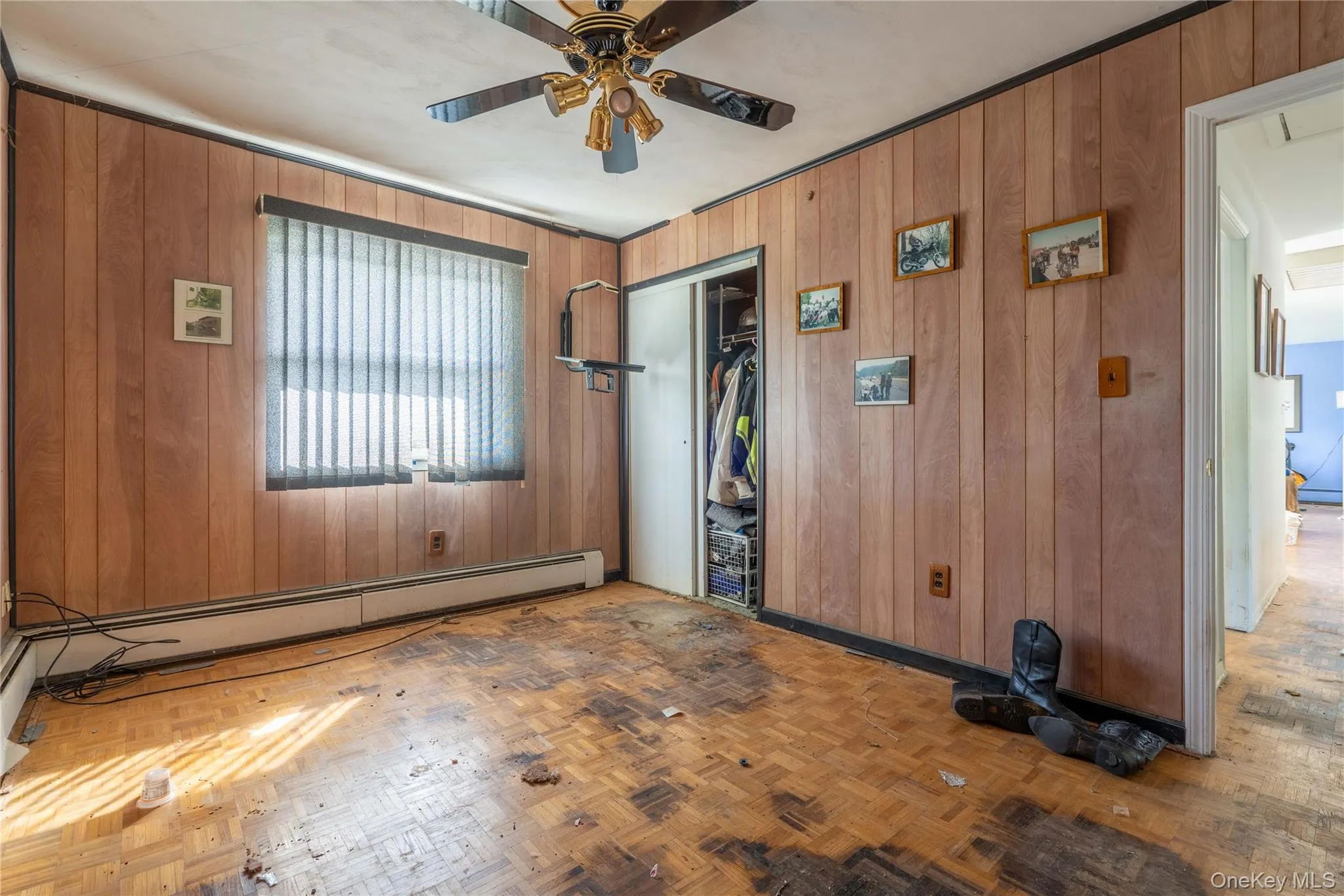 Spacious room featuring wood-finish parquet flooring, wood-paneled walls, and vertical blinds Spacious room featuring wood-finish parquet flooring, wood-paneled walls, and vertical blinds