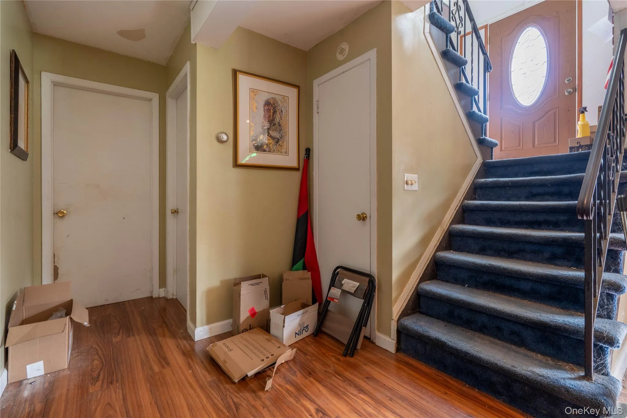 Welcoming foyer featuring wood-finish flooring, multiple closet storage, and a grand staircase with wrought iron railings and a circular skylight above Welcoming foyer featuring wood-finish flooring, multiple closet storage, and a grand staircase with wrought iron railings and a circular skylight above