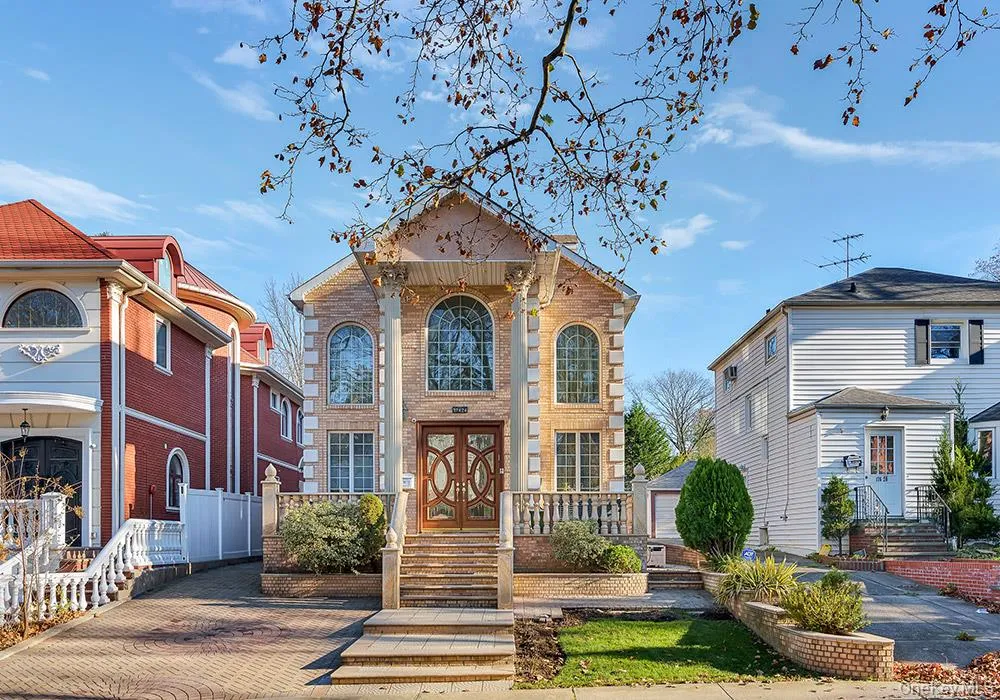 Brick exterior featuring a covered entryway with decorative columns, arched windows, stone-paved driveway, and a raised stone balcony with balustrade railings Brick exterior featuring a covered entryway with decorative columns, arched windows, stone-paved driveway, and a raised stone balcony with balustrade railings