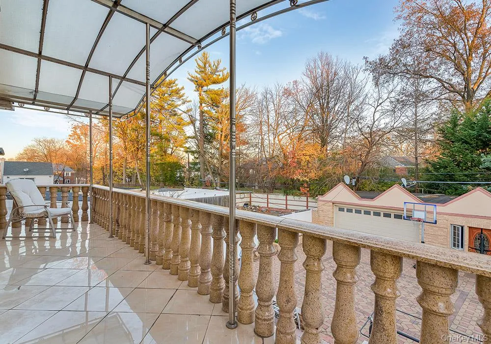 Covered terrace featuring stone-finish balustrades, large-format tile flooring, metal structural pillars, and a semi-translucent arched canopy Covered terrace featuring stone-finish balustrades, large-format tile flooring, metal structural pillars, and a semi-translucent arched canopy