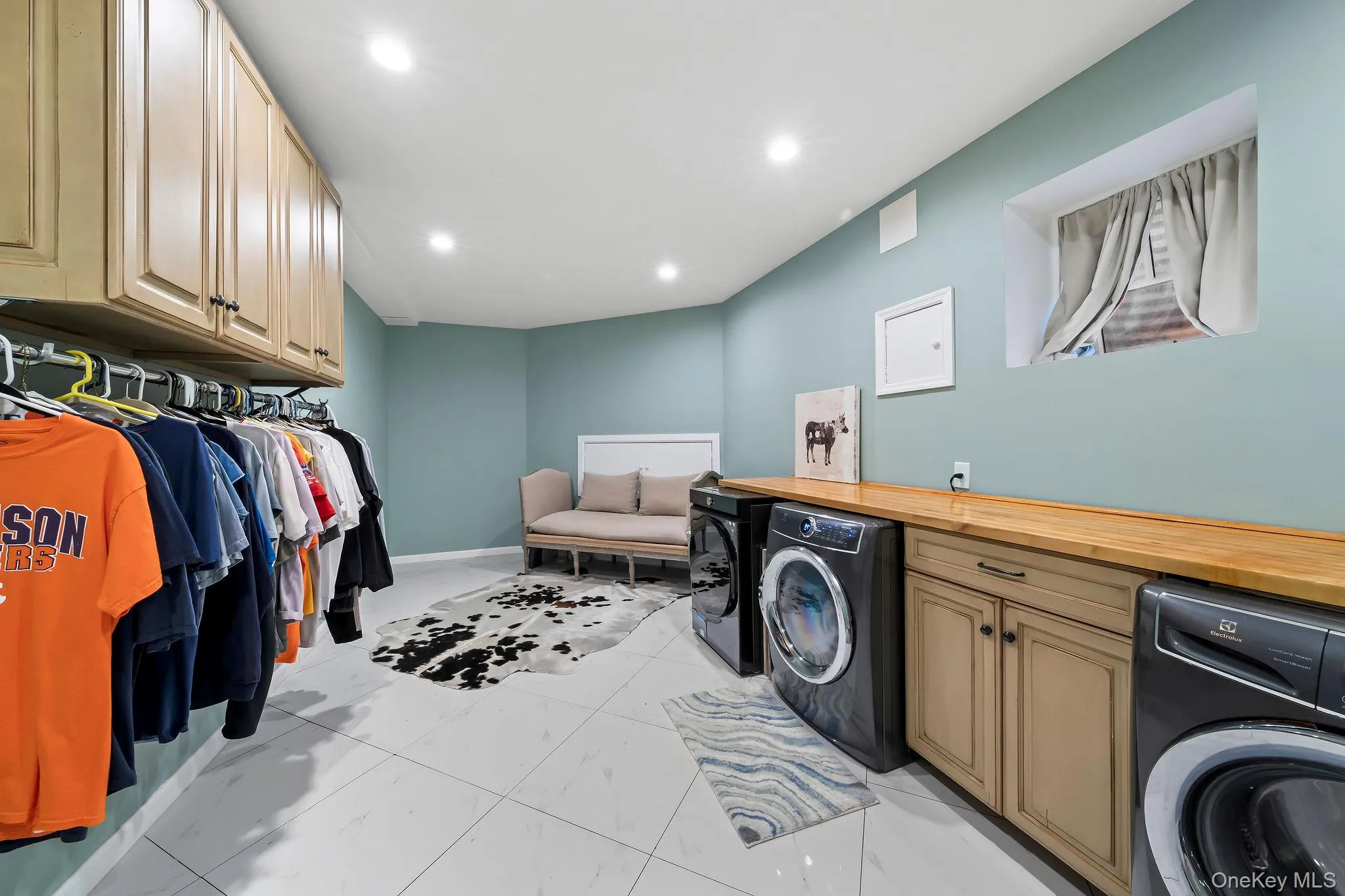 Dedicated laundry room featuring tile flooring, neutral wall-mounted cabinetry, an expansive wood-finish folding counter, and recessed lighting Dedicated laundry room featuring tile flooring, neutral wall-mounted cabinetry, an expansive wood-finish folding counter, and recessed lighting