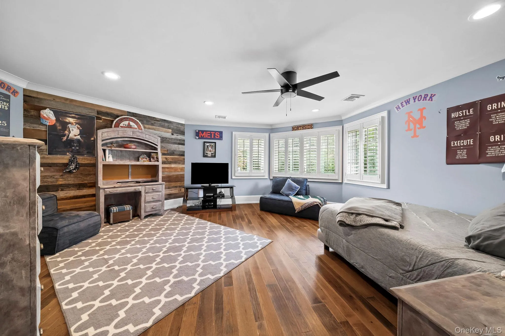 Wood-finish flooring, reclaimed wood-style plank accent wall, recessed lighting, matte black ceiling fan, and plantation shutters Wood-finish flooring, reclaimed wood-style plank accent wall, recessed lighting, matte black ceiling fan, and plantation shutters