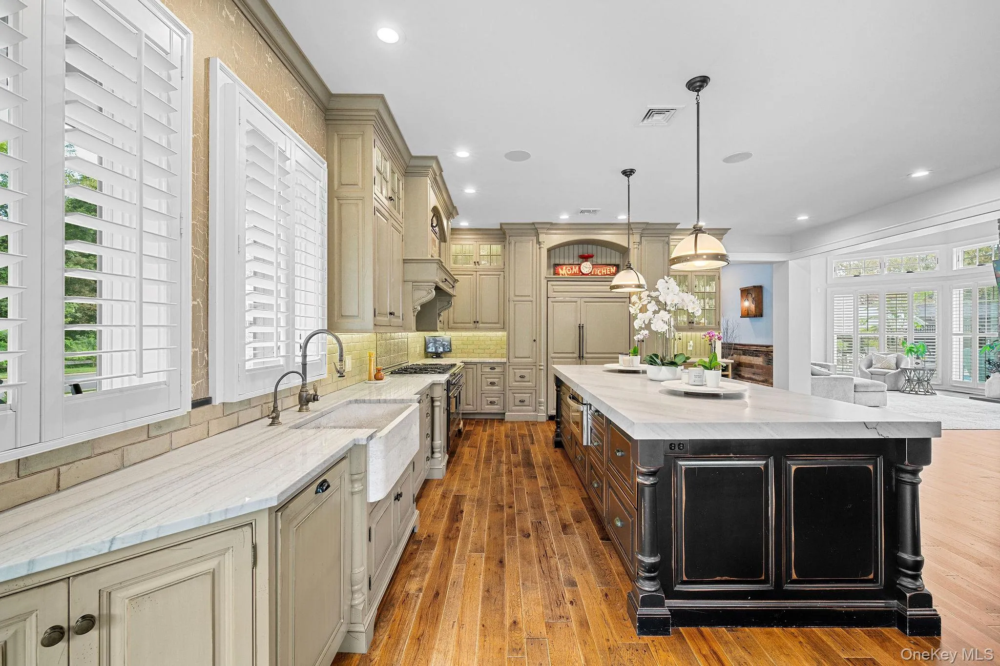 Kitchen featuring custom cabinetry, farmhouse-style sink, wood-finish flooring, stone-surfaced countertops, and a substantial center island Kitchen featuring custom cabinetry, farmhouse-style sink, wood-finish flooring, stone-surfaced countertops, and a substantial center island