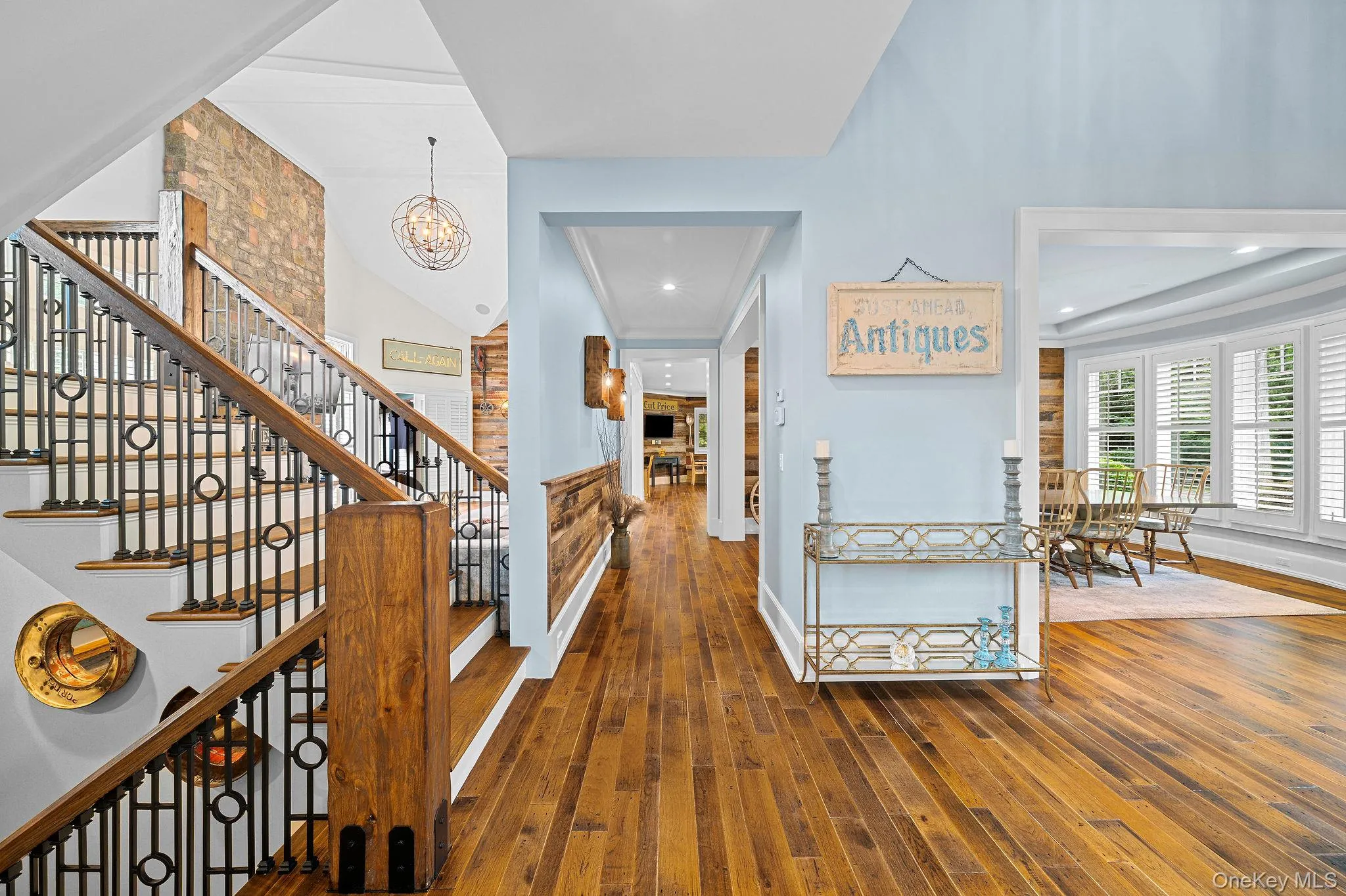 Interior featuring wood-finish flooring, a staircase with a metal railing and wood-tone newel post, an accent wall with stone masonry, horizontal wood-plank wainscoting, and recessed ceiling lighting Interior featuring wood-finish flooring, a staircase with a metal railing and wood-tone newel post, an accent wall with stone masonry, horizontal wood-plank wainscoting, and recessed ceiling lighting