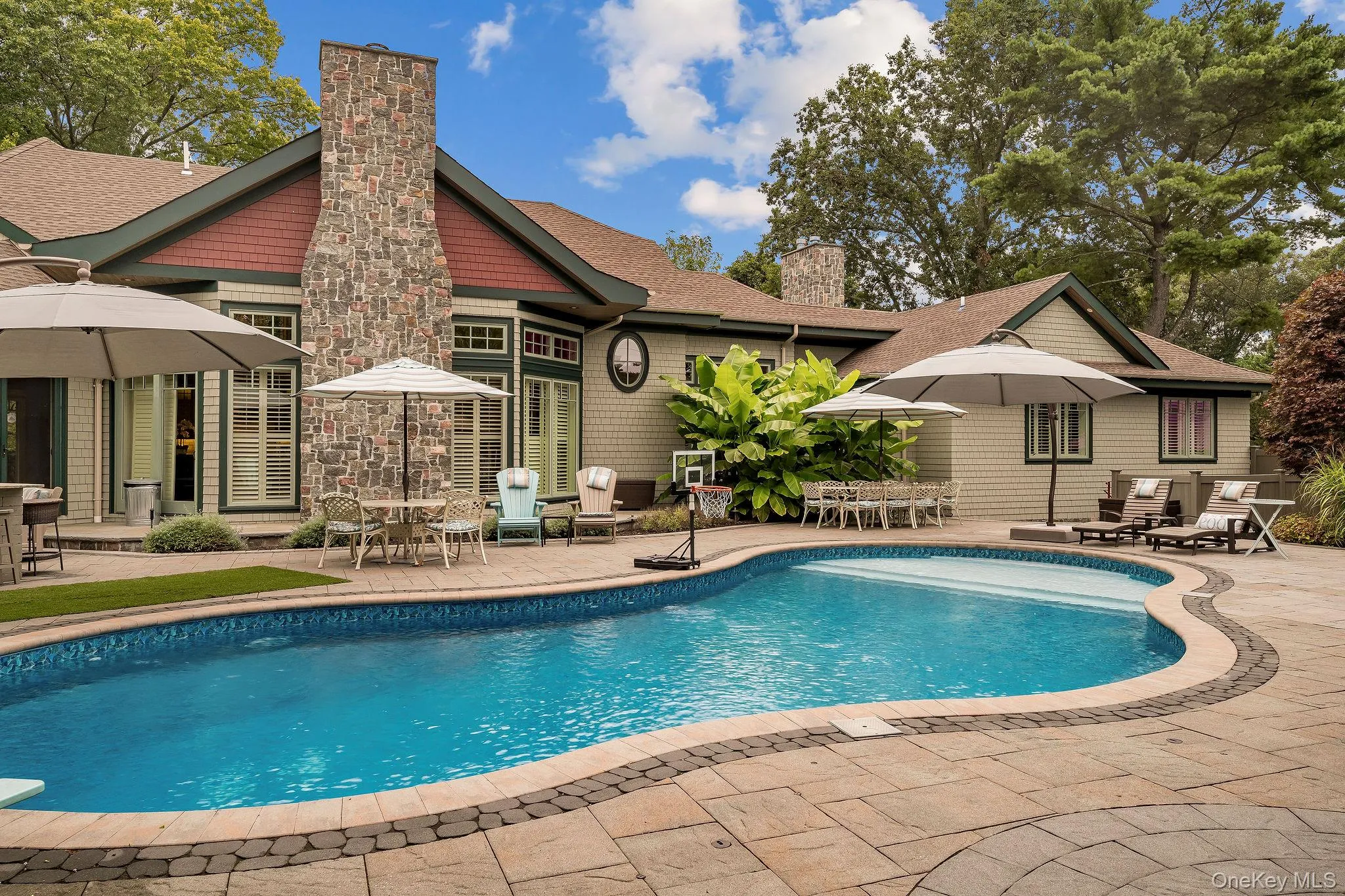 Custom-designed in-ground swimming pool with stone-tiled patio, stone exterior chimney, shingle-style siding, and extensive mature landscaping Custom-designed in-ground swimming pool with stone-tiled patio, stone exterior chimney, shingle-style siding, and extensive mature landscaping