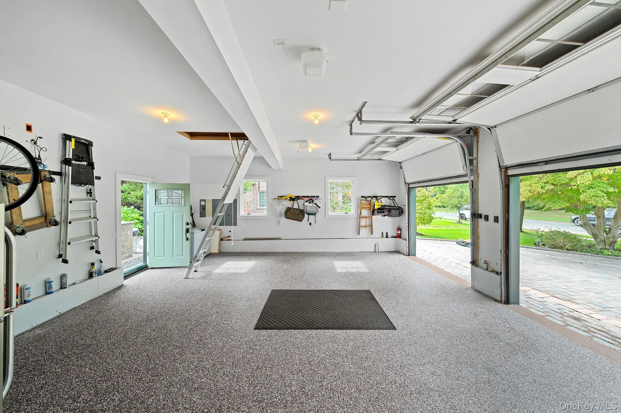 Multi-car garage featuring speckled epoxy flooring, overhead garage door system, integrated attic access ladder, and dual double-pane windows Multi-car garage featuring speckled epoxy flooring, overhead garage door system, integrated attic access ladder, and dual double-pane windows