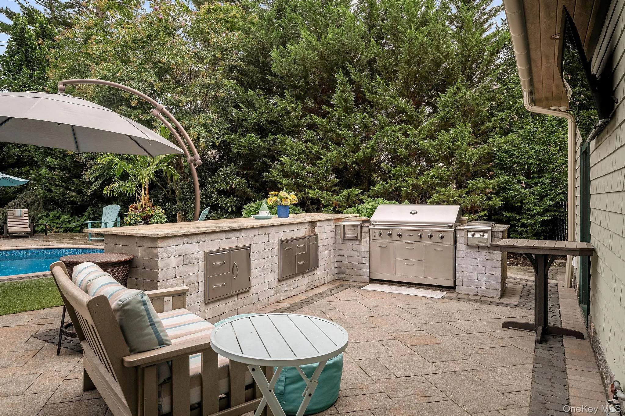 Outdoor kitchen featuring stone masonry, stainless steel built-in grill, stone-slab countertop, integrated storage cabinetry, and paver patio Outdoor kitchen featuring stone masonry, stainless steel built-in grill, stone-slab countertop, integrated storage cabinetry, and paver patio