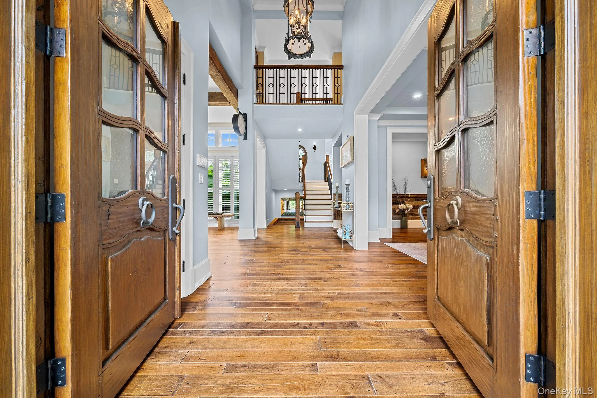 Double front doors featuring wood construction and glass inserts, wood-finish flooring, two-story ceiling height, intricate metal stair railing, and suspended foyer chandelier Double front doors featuring wood construction and glass inserts, wood-finish flooring, two-story ceiling height, intricate metal stair railing, and suspended foyer chandelier